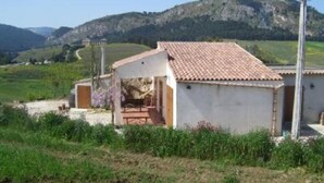 Un petit bâtiment d’un seul étage, doté d’un toit en tuiles, entouré de verdure et avec des collines en arrière-plan.