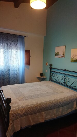 A bedroom with a bed, a nightstand, a wall-mounted lamp, and two framed pictures. - Sun House (Calatafimi Segesta)