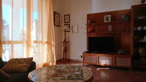Un salon comprenant un canapé, une table basse à motifs floraux, un téléviseur posé sur un meuble en bois et une bibliothèque contenant divers objets.