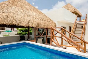 Une piscine dotée d’une terrasse en bois et de structures à toits de chaume.