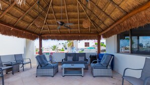 An outdoor patio with thatched roofing, wicker furniture, and a view of the cityscape. - Casa Mango Suite 3, Isla Mujeres. (Isla Mujeres)