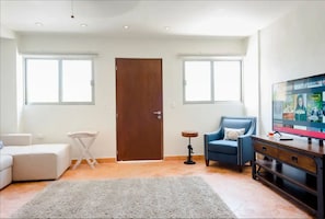 Un salon avec un canapé, un fauteuil bleu, un téléviseur et un meuble en bois.