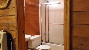 Een badkamer met een houten wand, een wit toilet en een douchecabine.