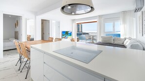A modern kitchen with a central island, dining area with chairs, a sofa, and a balcony with a view. - Veracruz 11-B (Benidorm)