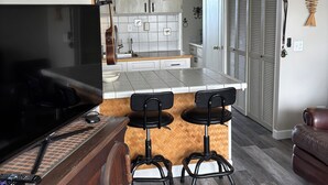 Ein modernes Wohnzimmer mit Fernseher, Holzmöbeln, einem gemusterten Teppich und einer Küchenzeile mit Bar.