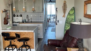Eine moderne Küche mit Pendelleuchten, ein Essbereich mit Ledersesseln, einer Surfbrettrückwand und Blick auf einen Balkon.