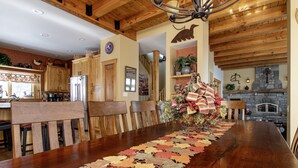 A wooden dining table with a leaf-patterned runner, wooden chairs, a chandelier, and a stone fireplace. - Luxury 6br Solitude Ge- Indoor Bball Court, Private Tub 6 Bedroom Home by RedAwning (Ludlow)
