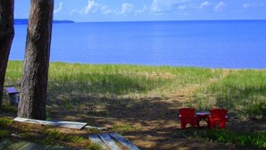 A beach view with a clear sky, a calm sea, and two red chairs on the sand.