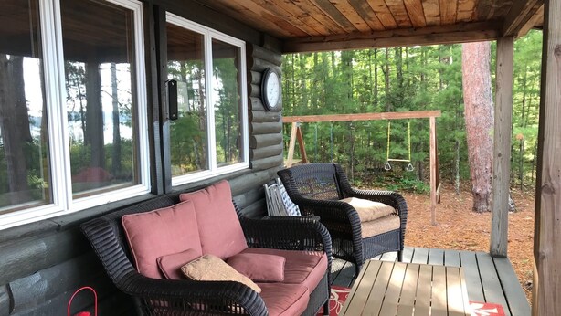 A log cabin with a porch, wicker furniture, a swing set, and a red lantern.