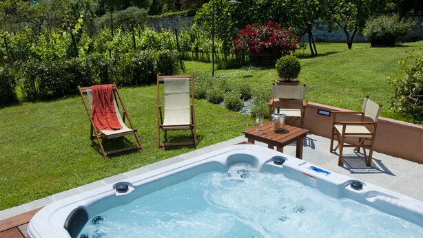 Un jacuzzi con cubierta de madera, rodeado por un jardín exuberante con diversas plantas y un pequeño arroyo.