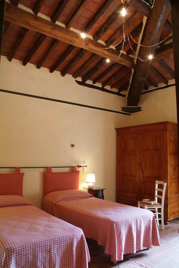 Una habitación con dos camas, un armario de madera, una silla y una lámpara colgante.