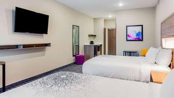 A hotel room with two beds, a flat-screen TV mounted on the wall, a small desk with a lamp, and a colorful abstract painting on the wall.