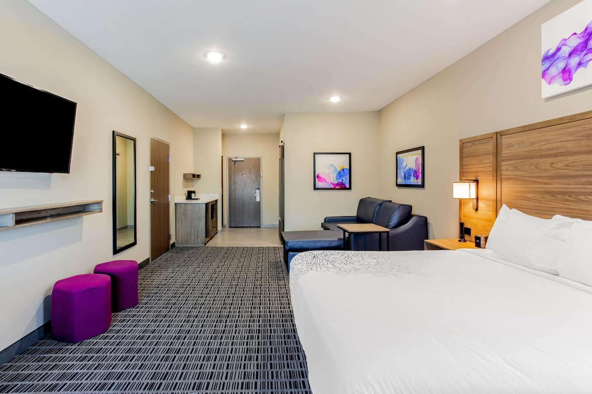 Une chambre d’hôtel avec un grand lit, un bureau, une chaise, un canapé, une télévision et une salle de bain visible à travers une porte ouverte.