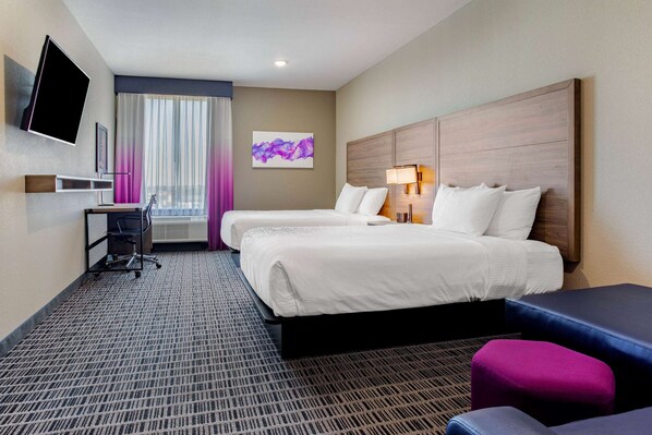 A hotel room with two beds, a desk, a TV, and a window with curtains.