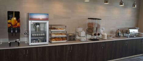 A breakfast bar with a coffee machine, juice dispenser, and various food items.
