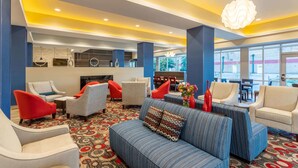 A modern lobby with a patterned carpet, seating area with sofas and armchairs, a reception desk, and large windows offering a view.