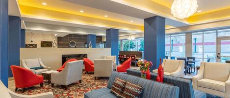 A modern lobby with a patterned carpet, seating area with sofas and armchairs, a reception desk, and large windows offering a view.