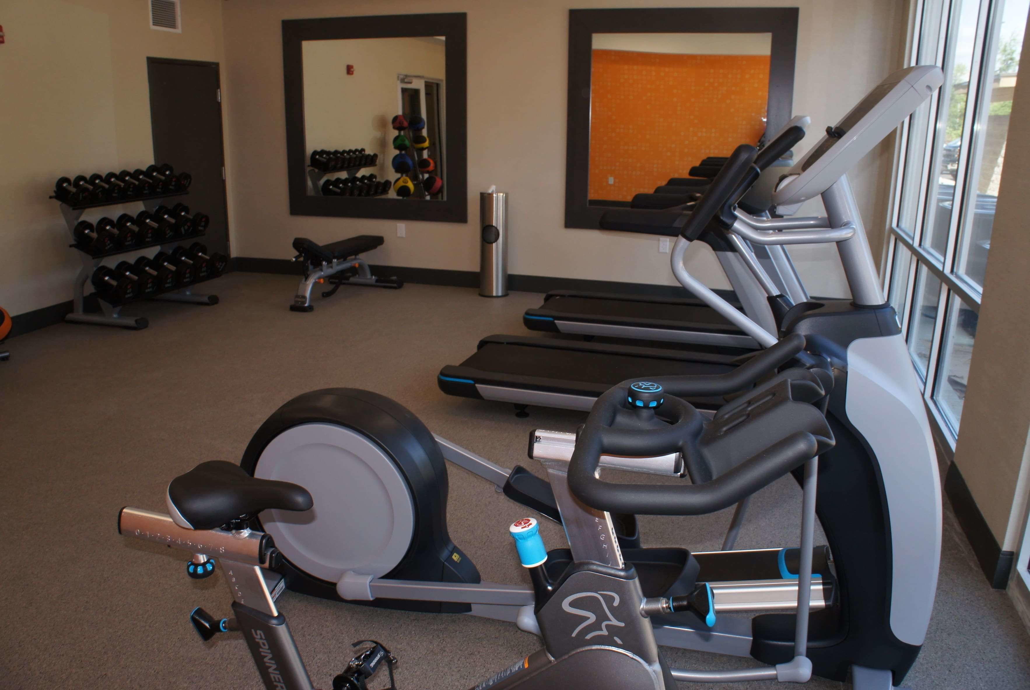 A gym with exercise equipment, including treadmills, a stationary bike, and dumbbells.