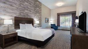 A hotel room with a large bed, two bedside tables with lamps, a flat-screen TV, a desk with a chair, and a large window with curtains.