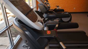 Una fila de bicicletas estáticas, con pantallas digitales, ubicadas en una habitación con pared naranja y ventanas amplias.