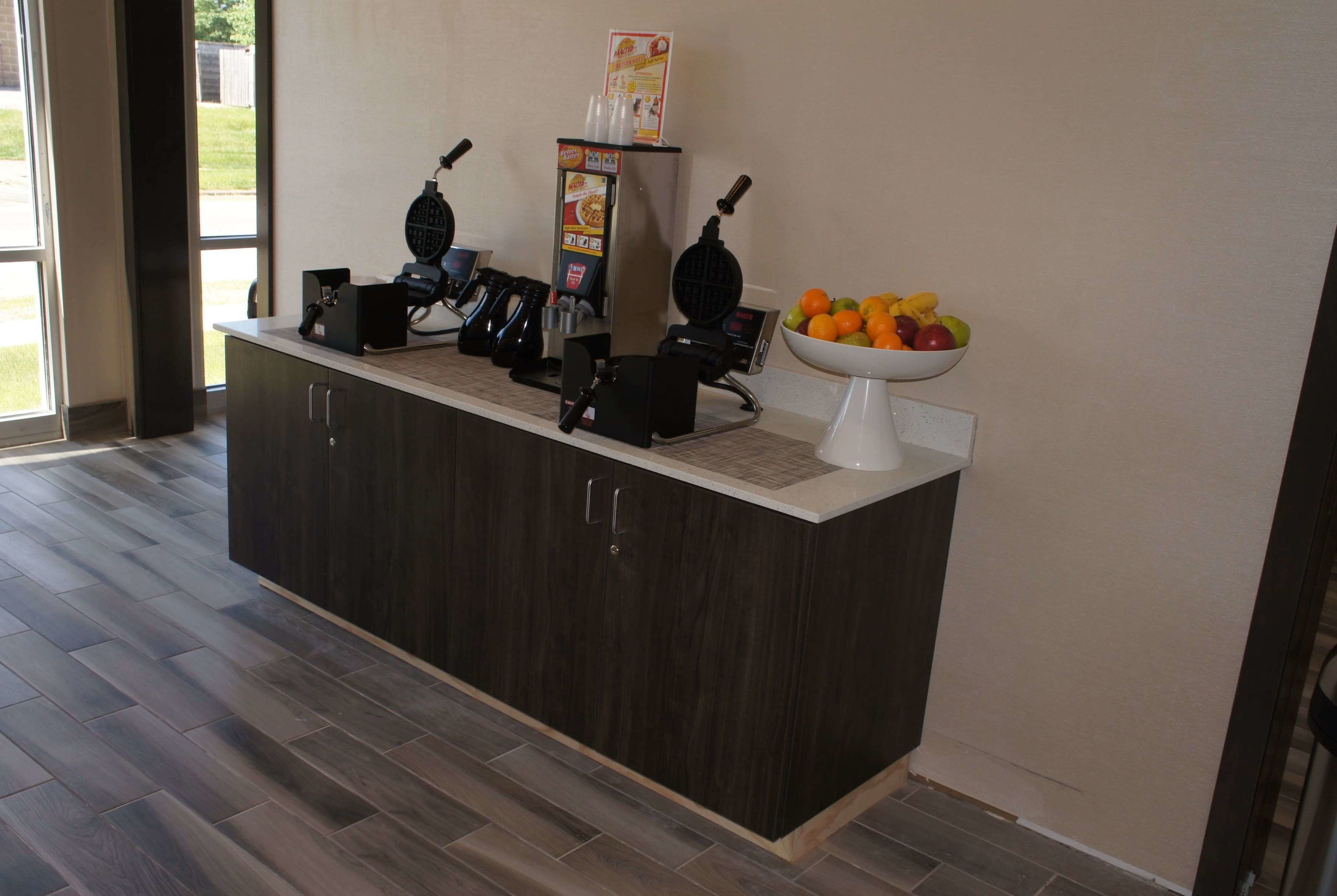 Una cocina con un mostrador de madera oscura, un fabricante de gofres, una cafetera y un bol de fruta.