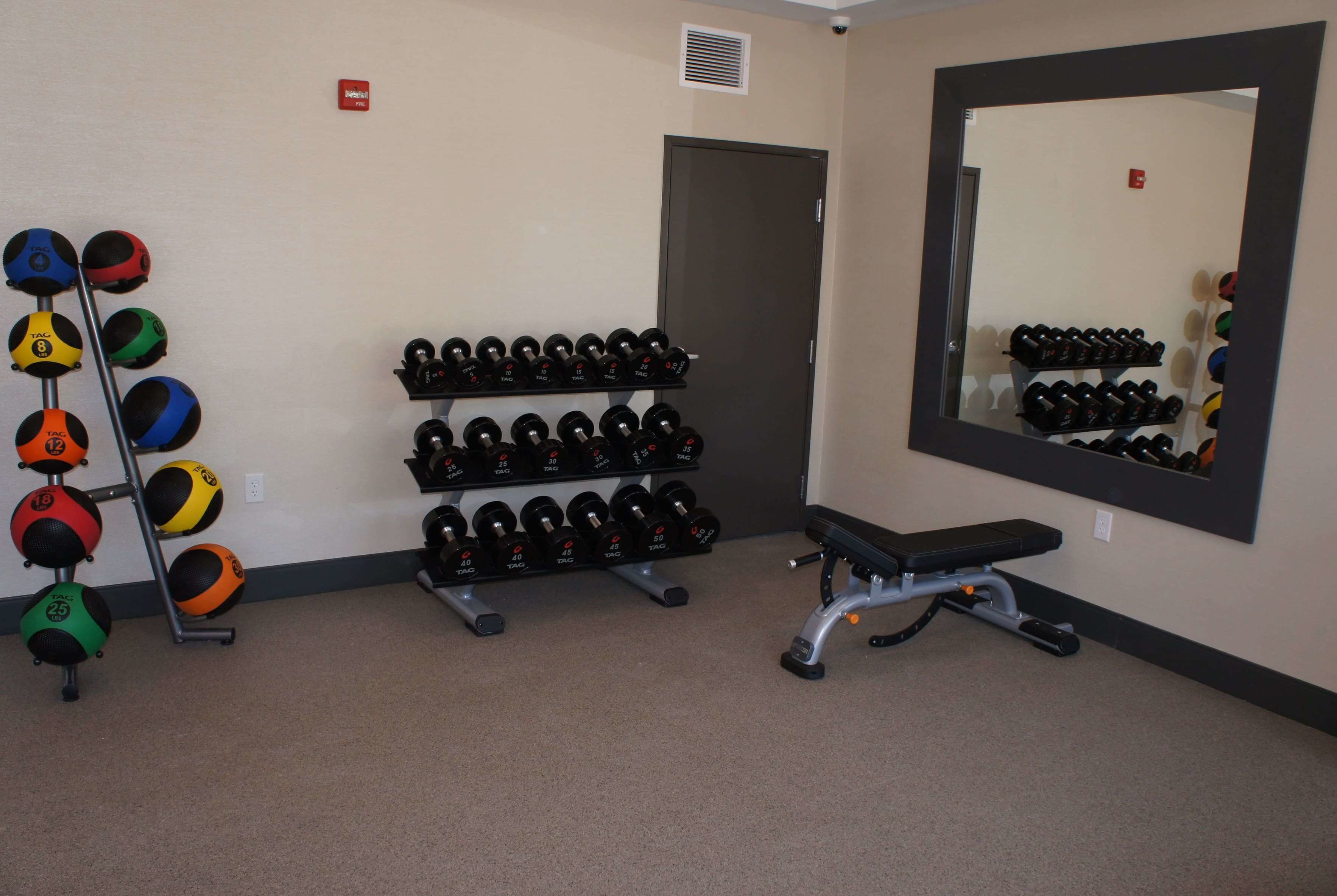 A gym with weightlifting equipment, a bench, and a mirror.