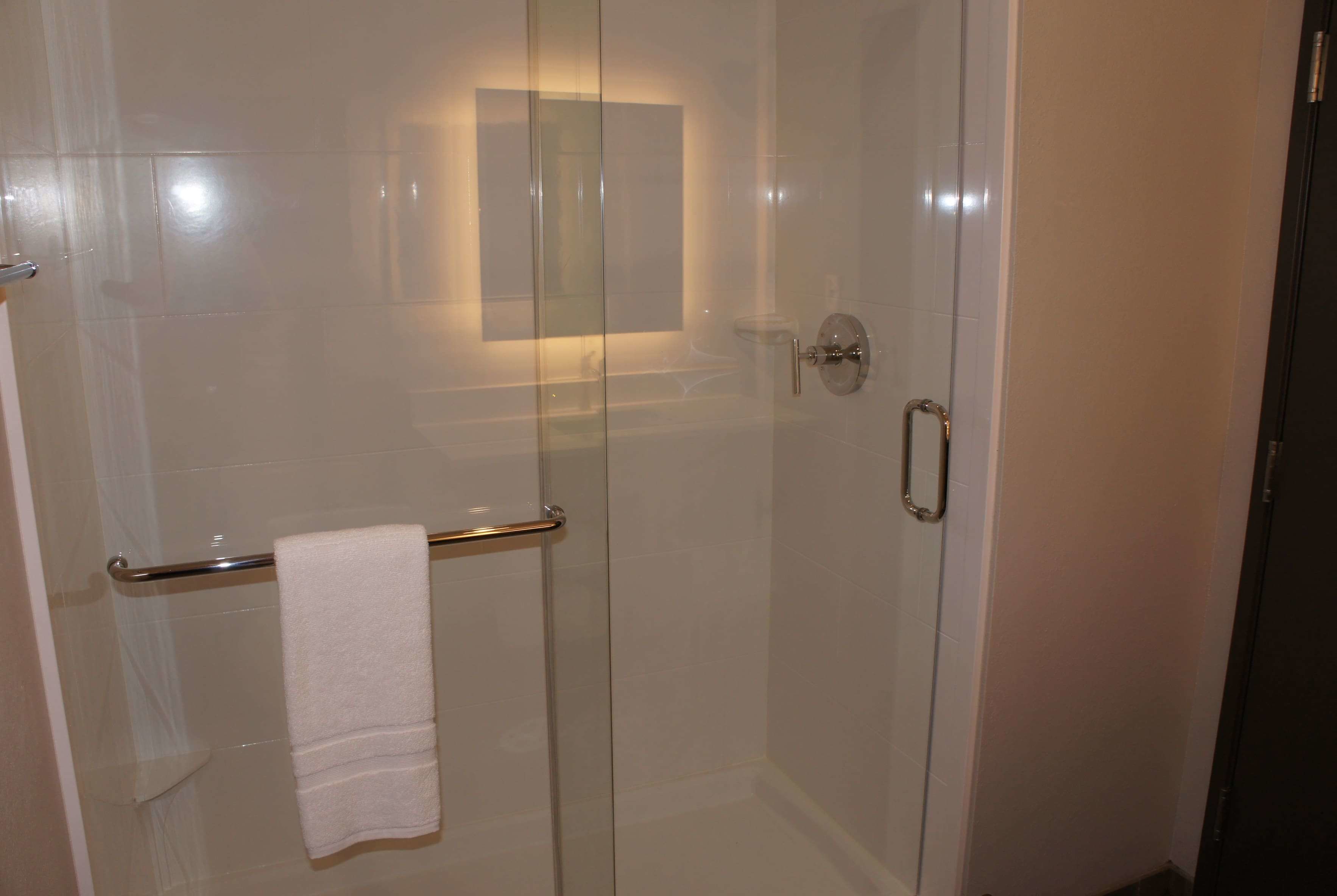 A glass-enclosed shower with a towel rack and a small mirror.