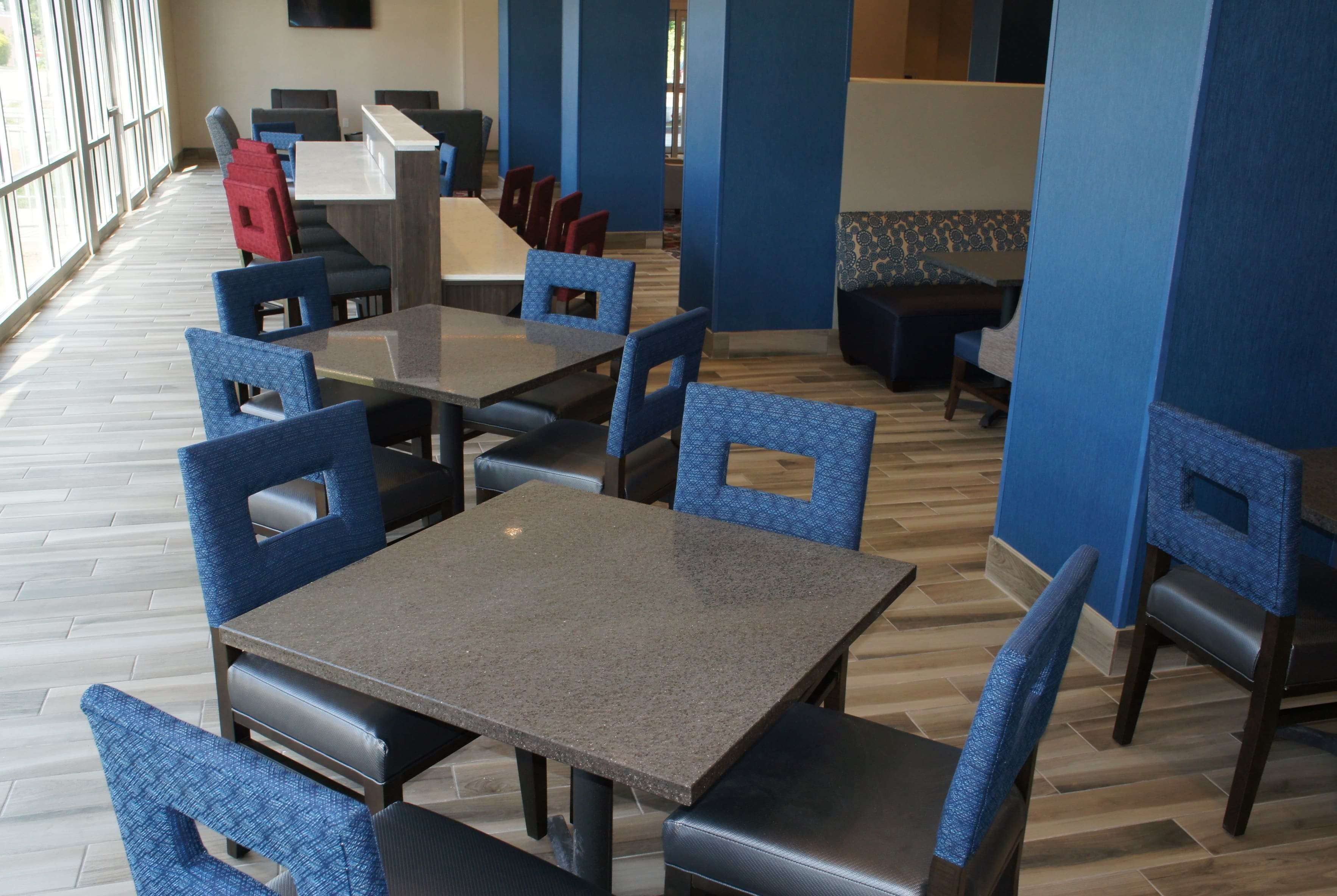 A restaurant with blue upholstered chairs and tables, wooden flooring, and large windows.