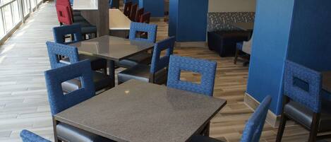 A restaurant with blue upholstered chairs and tables, wooden flooring, and large windows.