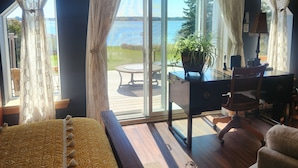 Een kamer met een bed, een bureau en uitzicht op een terras en water.