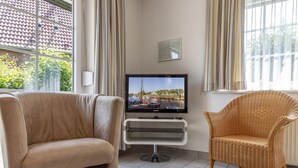 A living room with a television, two chairs, and a view of a coastal area through large windows. - Timeless and elegant: the semi-detached house impresses with both its brightness (Carolinensiel)