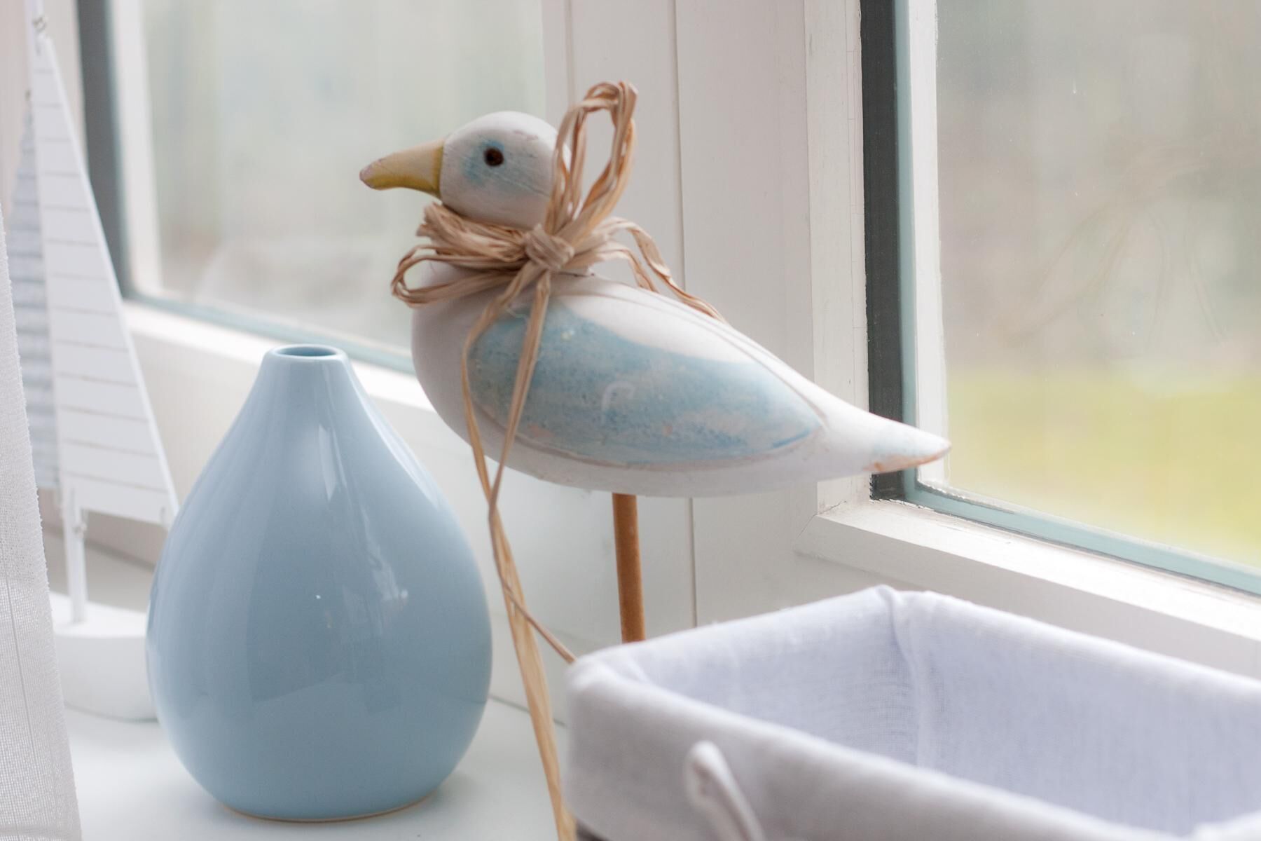 Una decorazione a forma di uccello legata con uno spago, un vaso azzurro e una culla bianca.