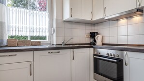 A modern kitchen with white cabinets, a Bosch oven, and a window with white curtains. - Timeless and elegant: the semi-detached house impresses with both its brightness (Carolinensiel)