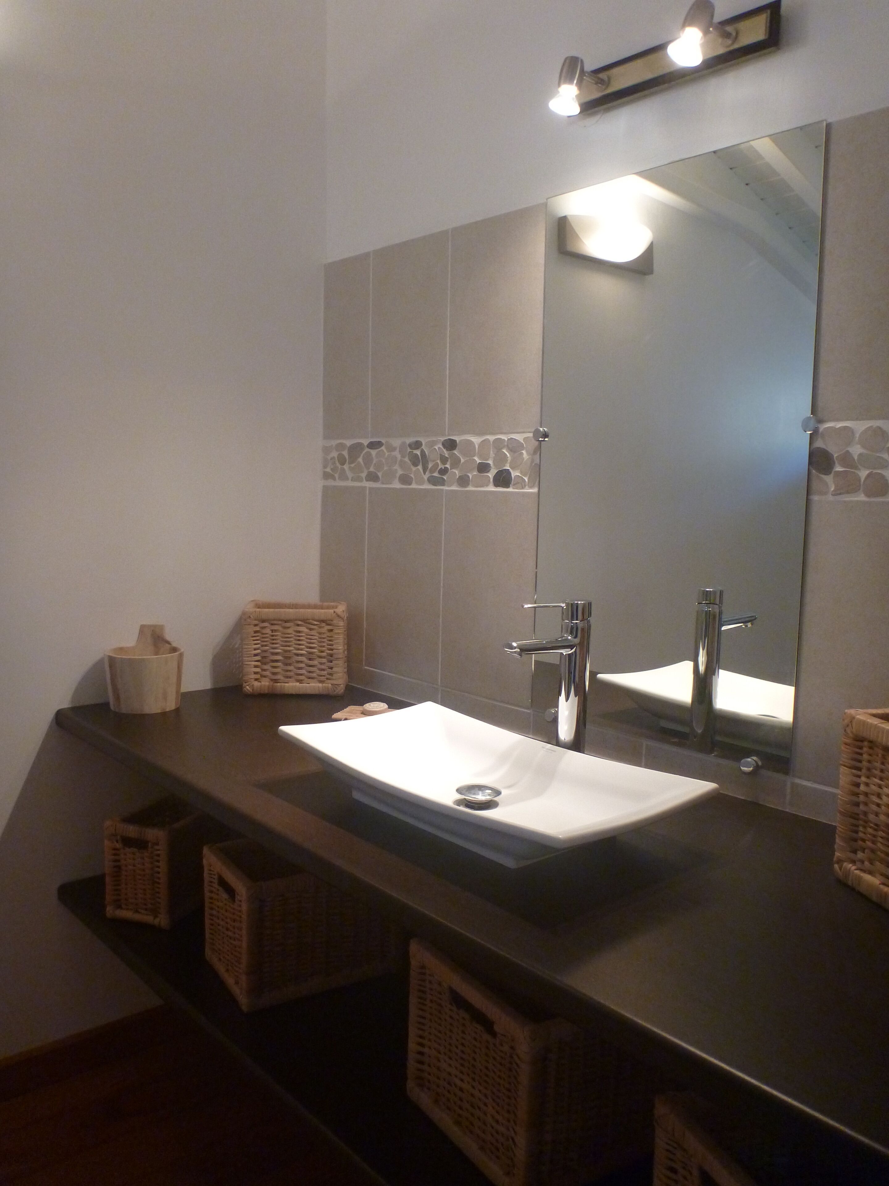 Une salle de bain avec un grand miroir, un lavabo blanc et deux paniers en osier posés sur le comptoir.