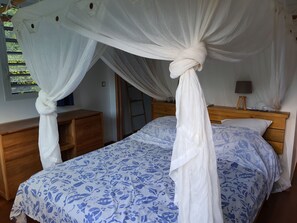 A bedroom with a canopy bed, wooden headboard, bedside table, and a lamp.