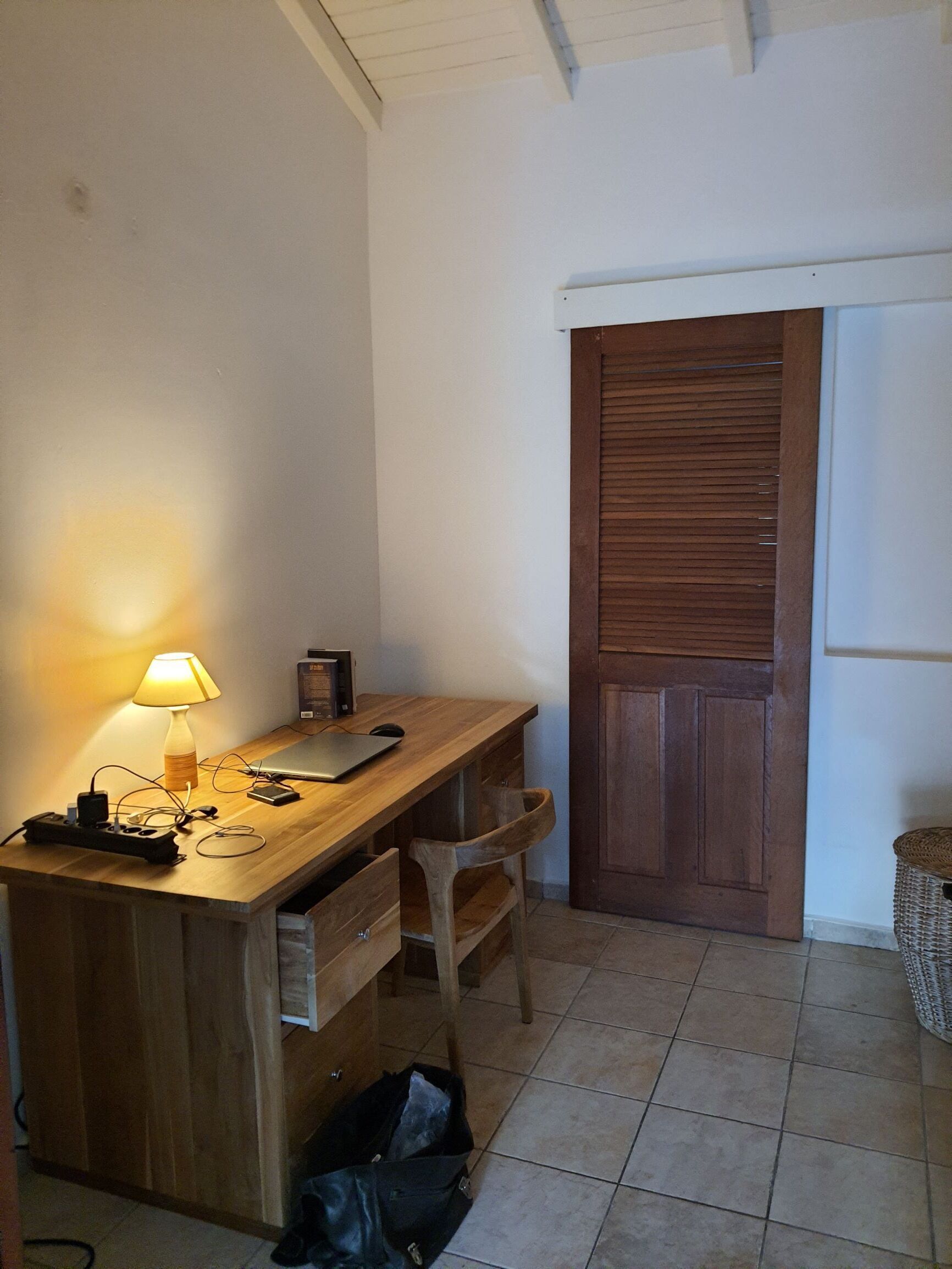 A small room with a wooden desk, a lamp, a laptop, and a closed door.