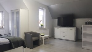 Um quarto moderno com cama, escrivaninha, televisão e guarda-roupa.