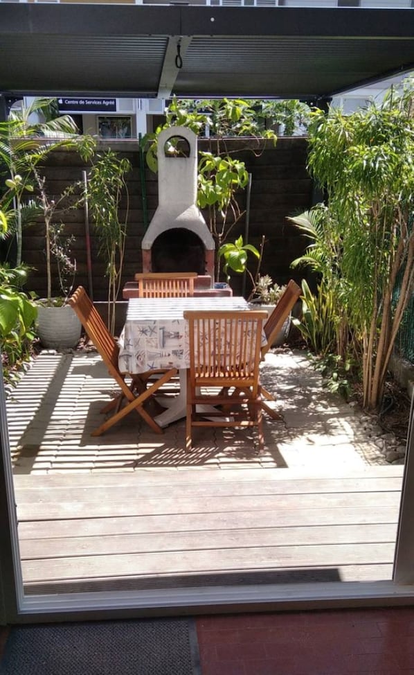 An outdoor patio with a wooden table and chairs, a pizza oven, and various plants. - Ground level apartment equipped for 4 persons 109 yards from the Hermitage beach (Saint Gilles Les Bains)