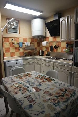 A kitchen with a table covered in a floral tablecloth, a dishwasher, a stove, and cabinets.