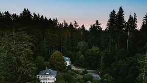 A large house surrounded by dense forest, with a small dock and sailboats visible. - Gorgeous location and getaway! Pickleball court! (Lakebay)