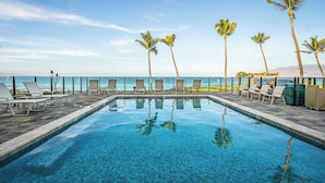 A swimming pool with lounge chairs and palm trees, overlooking a beach and ocean.