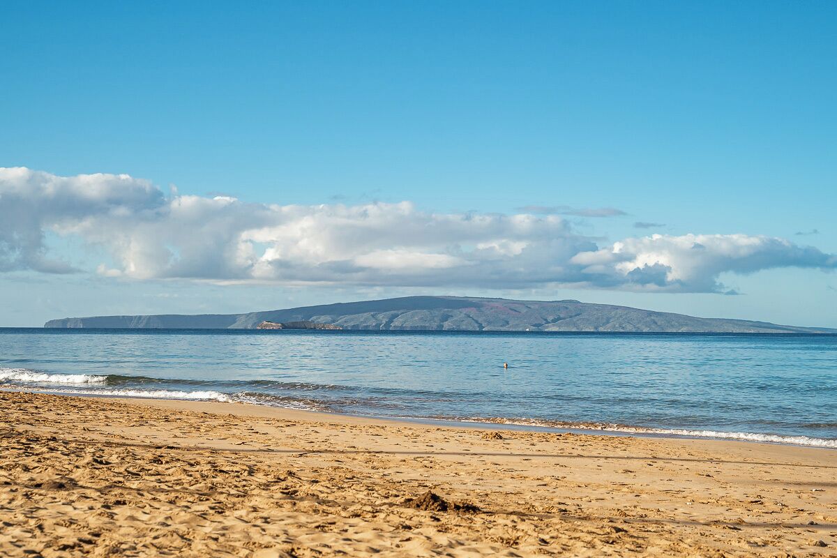 A beach with a clear view of a distant mountain range under a blue sky.