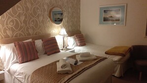 Habitación de hotel con cama, almohadas, lámpara de noche, espejo, cuadro y una silla.