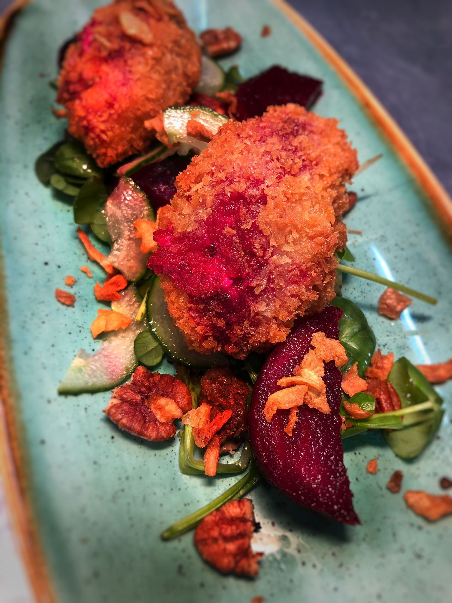 A dish with breaded balls, beetroot, and greens on a speckled plate.