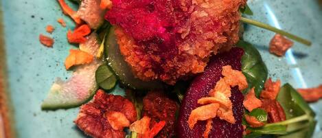A dish with breaded balls, beetroot, and greens on a speckled plate.