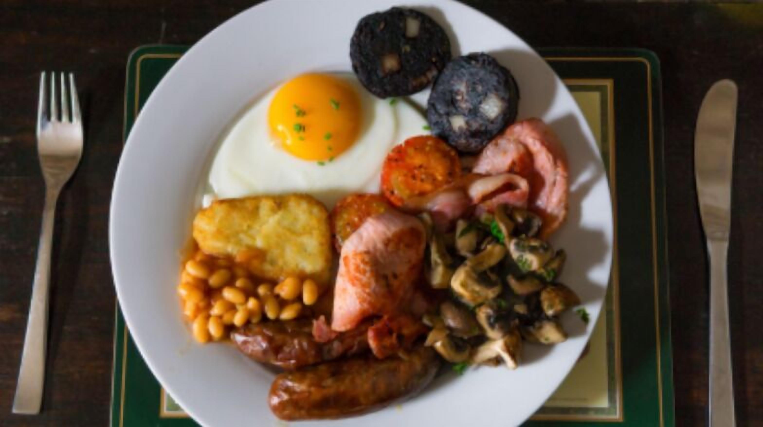 Un plato de comida para el desayuno con huevos, salchichas, champiñones, frijoles y morcilla.