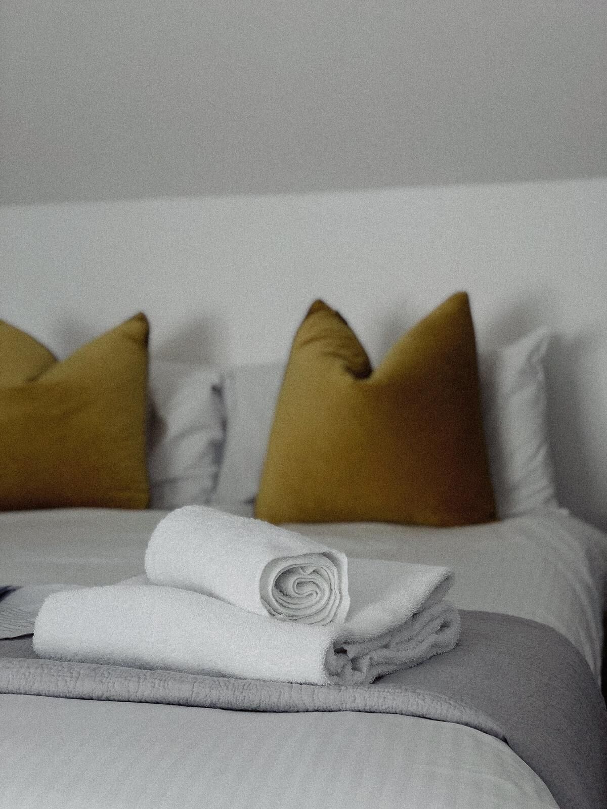 A neatly made bed with a rolled white towel and two mustard-colored pillows.