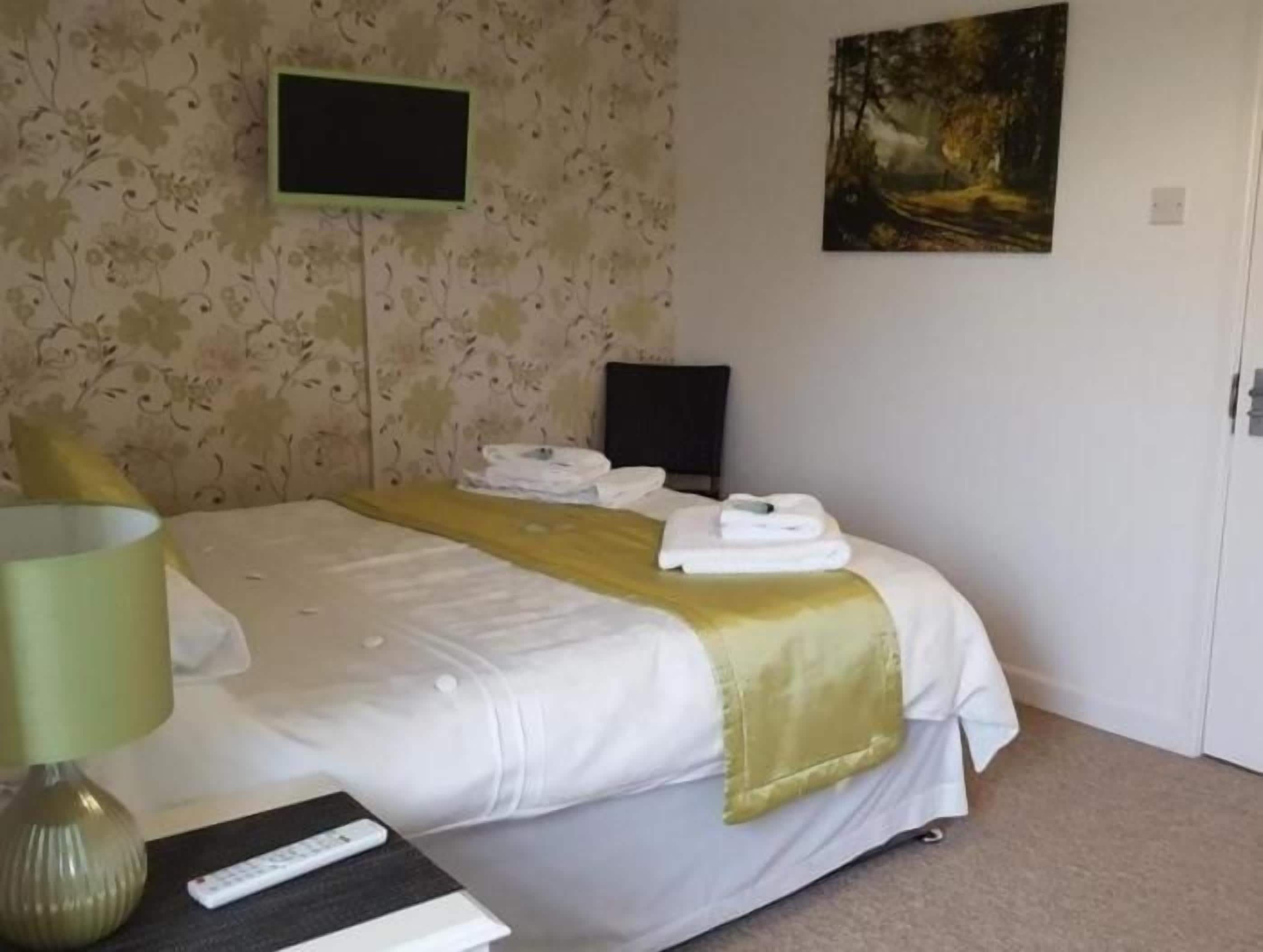 A hotel room with a bed, a flat-screen TV, a painting on the wall, and a door.