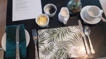 A table set with a green napkin, a fork, a knife, a spoon, a teapot, a cup, and a small bowl of butter.