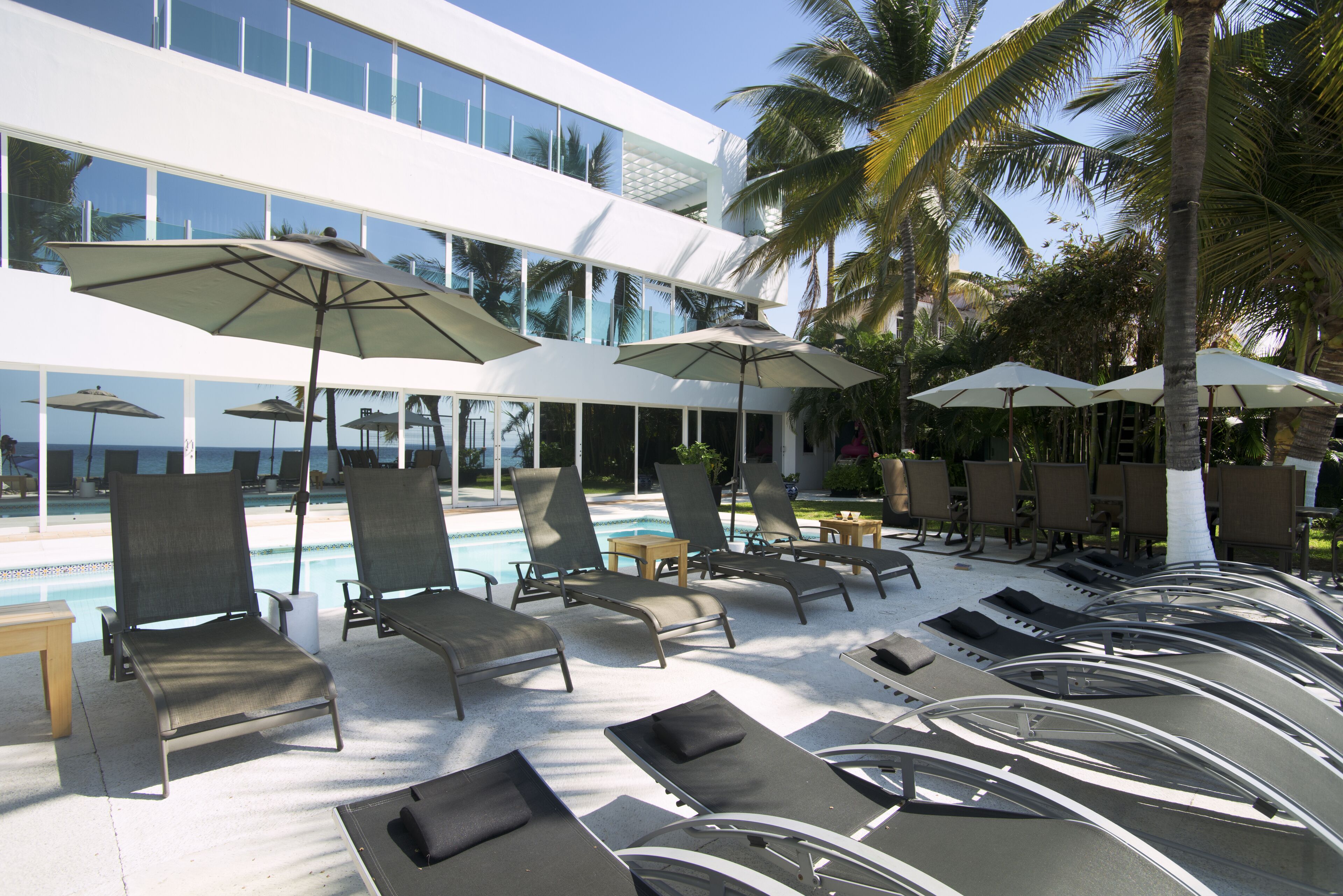 A poolside area with lounge chairs and umbrellas, a pool, and a modern building in the background.